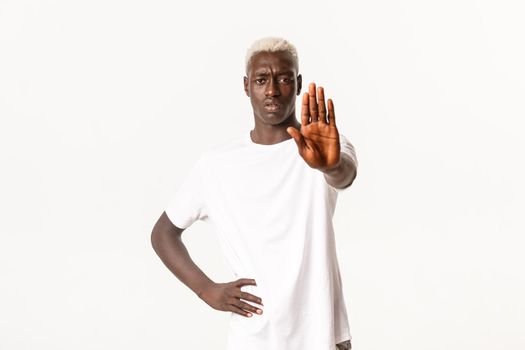Portrait of displeased african-american blond man, extend hand and showing stop gesture, restrict something, prohibit action, standing white background.