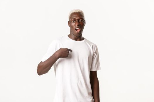 Portrait of sassy african-american blond man, pointing at himself and swearing, standing white background arrogant.