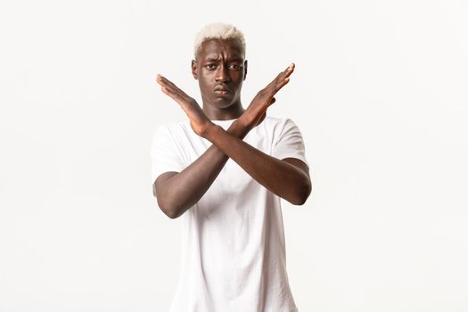 Portrait of serious african-american blond man, making cross gesture to stop something bad, disapprove action, prohibit, standing white background.