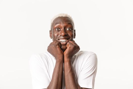 Close-up of cheerful handsome african-american blond male, looking with temptation and admiration, smiling amazed, standing white background.