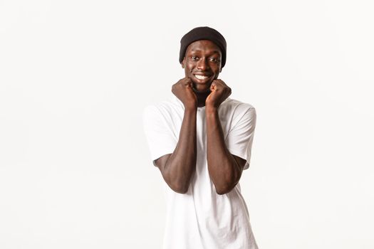 Portrait of upbeat cute and silly african-american guy looking adorable and smiling, wearing beanie with t-shirt, standing white background.