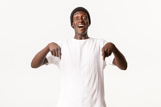 Portrait of excited and upbeat handsome african-american male, pointing fingers down and smiling amazed, white background.