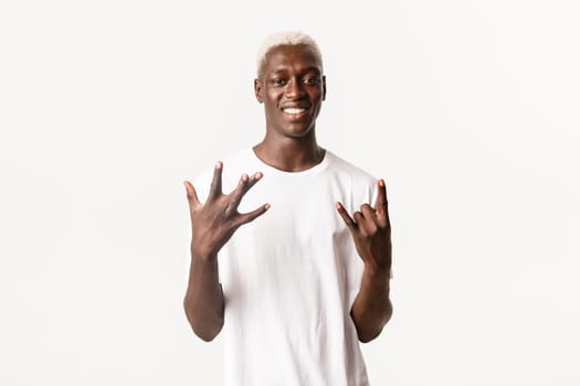 Portrait of stylish african-american blond guy showing west coast hand sign and rock-on, smiling upbeat, standing white background.