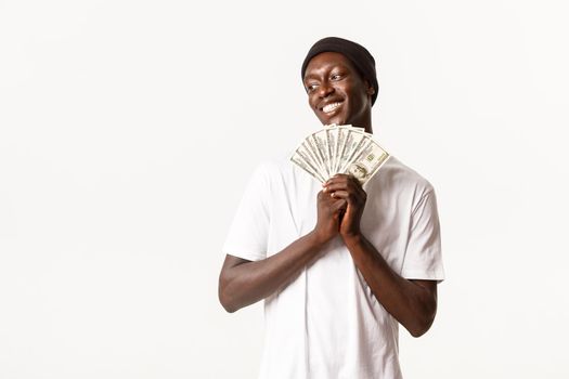 Portrait of delighted smiling african-american young man got lucky, holding money prize and looking away satisfied, white background.