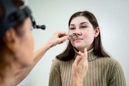 Professional female doctor otorhinolaryngologist doing nose examination with otoscope in modern hospital. Nasal congestion, sinusitis, allergy concept. Woman ENT doctor and patient in office clinics.