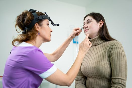 Female ENT doctor examines patient's sinuses with medical instrument in modern clinic. Otorhinolaryngologist checks the patient's girl's nose for diseases, allergies and curvature of the nasal septum.