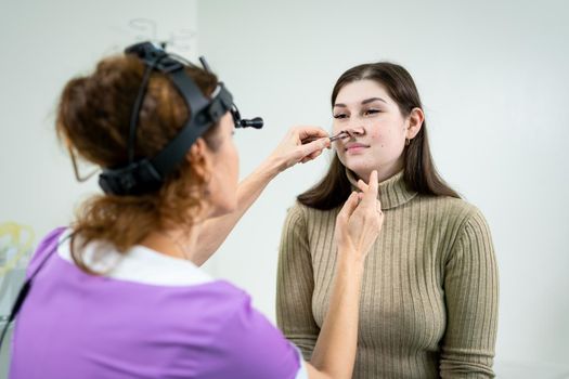 Otolaryngology concept. Positive woman otorhinolaryngologist checking nose with otoscope of his patient at hospital. Nasal congestion, sinusitis, allergy concept. Female patient at modern ENT clinic.