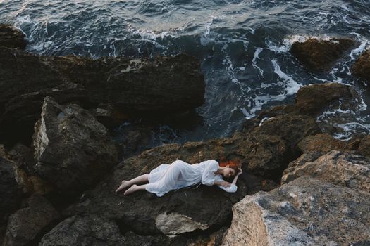 attractive woman with long hair in a secluded spot on a wild rocky coast in a white dress unaltered. High quality photo