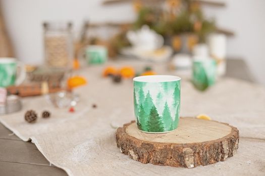 Winter table decor , on a linen tablecloth there is a green mug of hot drink on a tree cut.