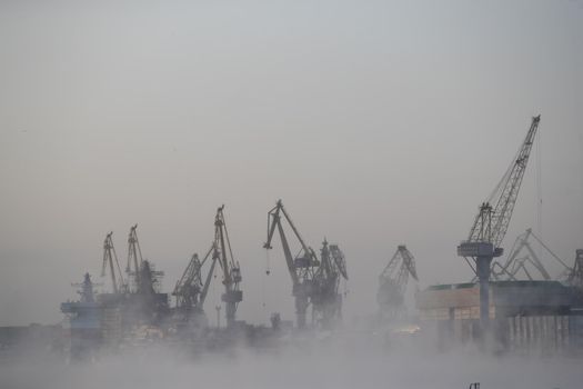 The construction of nuclear icebreakers, cranes of of the Baltic shipyard in a frosty winter day, steam over the Neva river, smooth surface of the river. High quality photo