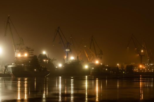 The construction of nuclear icebreakers at night, cranes of of the Baltic shipyard in a frosty winter day, steam over the Neva river, smooth surface of the river, fog. High quality photo