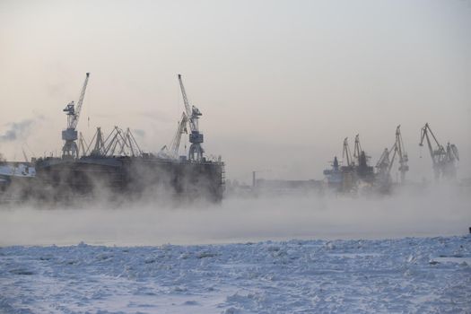 The construction of nuclear icebreakers, cranes of of the Baltic shipyard in a frosty winter day, steam over the Neva river, smooth surface of the river. High quality photo