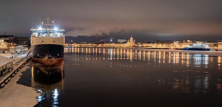 The panoramic footage of the winter night city Saint-Petersburg with picturesque reflection on water, big ship moored near Blagoveshchensky bridge, English embankment, cathedral on background. High quality photo