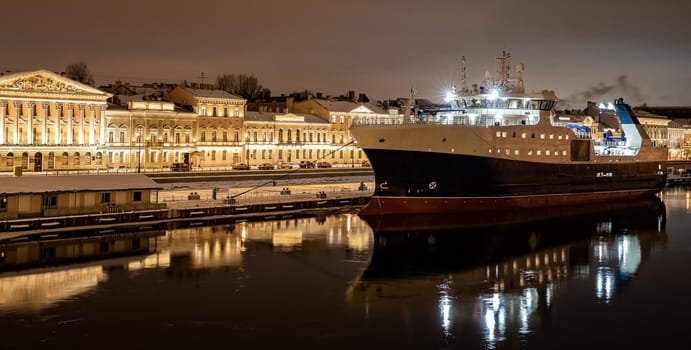 The panoramic footage of the winter night city Saint-Petersburg with picturesque reflection on water, big ship moored near Blagoveshchensky bridge or lieutenant Schmidt, Isaac cathedral on background. High quality photo