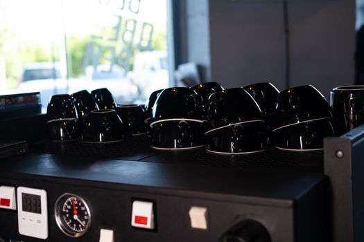 Pile of empty clean black coffee cups mugs on shelf or coffee machine in cafe indoors.