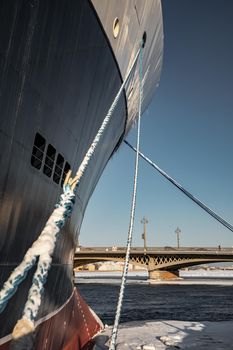 The panoramic view of the winter city Saint-Petersburg at sunny day, big ship moored near Blagoveshchensky bridge, mooring lines, thick ropes, river and bridge on background. High quality photo