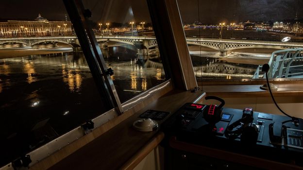 The panoramic view from cabin of ship of the winter night city Saint-Petersburg with picturesque reflection on water, big ship moored near Blagoveshchensky bridge or lieutenant Schmidt. High quality photo