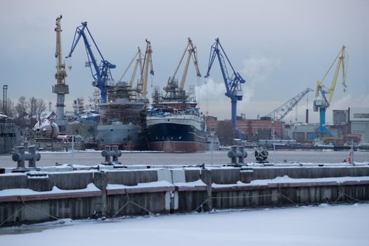 The construction of nuclear icebreakers, cranes of of the Baltic shipyard in a frosty winter day, steam over the Neva river, smooth surface of the river. High quality photo