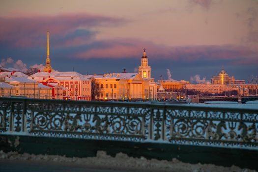 Winter panoramic view of St. Petersburg at sunset, golden spire of Peter and Paul fortress, Kunstkamera tower, embankment with bridge on background, steam over frozen Neva river, sky of orange color. High quality photo