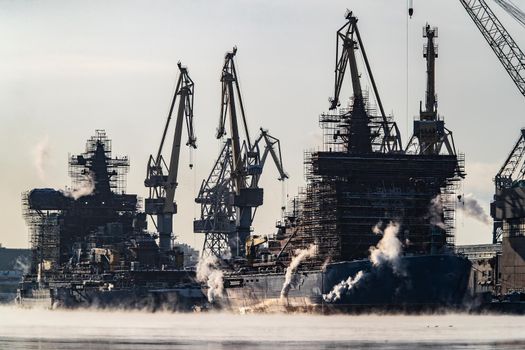 The construction of nuclear icebreakers, cranes of of the Baltic shipyard in a frosty winter day, steam over the Neva river, smooth surface of the river. High quality photo