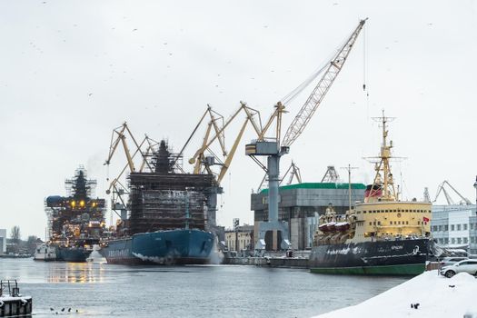 Russia, St. Petersburg, 05 February 2021: The construction of nuclear icebreakers, cranes of of the Baltic shipyard in a frosty winter day, steam over the Neva river, smooth surface of the river. High quality photo
