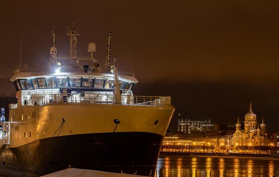 The panoramic footage of the winter night city Saint-Petersburg with picturesque reflection on water, big ship moored near Blagoveshchensky bridge, English embankment, cathedral on background. High quality photo