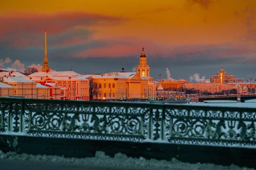 Winter panoramic view of St. Petersburg at sunset, golden spire of Peter and Paul fortress, Kunstkamera tower, embankment with bridge on background, steam over frozen Neva river, sky of orange color. High quality photo