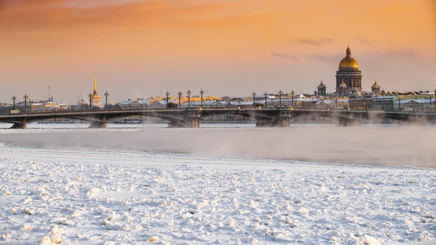 Winter panoramic view of St. Petersburg at sunset, Isaac cathedral and Blagoveshenskiy bridge on background, steam over frozen Neva river, sky of orange color. High quality photo