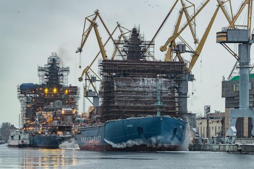 Russia, St. Petersburg, 05 February 2021: The construction of nuclear icebreakers, cranes of of the Baltic shipyard in a frosty winter day, steam over the Neva river, smooth surface of the river. High quality photo