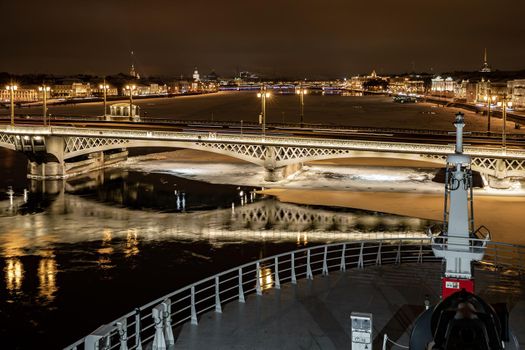 The panoramic view from cabin of ship of the winter night city Saint-Petersburg with picturesque reflection on water, big ship moored near Blagoveshchensky bridge or lieutenant Schmidt. High quality photo