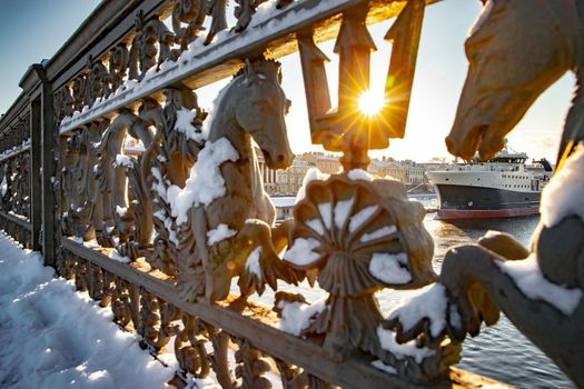 The big ship moored near English embankment through the railing of the bridge Blagoveshchensky, the winter city Saint-Petersburg, the lights of a sun, mooring lines, thick ropes. High quality photo