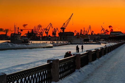The construction of nuclear icebreakers at magic sunset, cranes of of the Baltic shipyard in a frosty winter day, steam over the Neva river, smooth surface of the river, sky of orange color. High quality photo