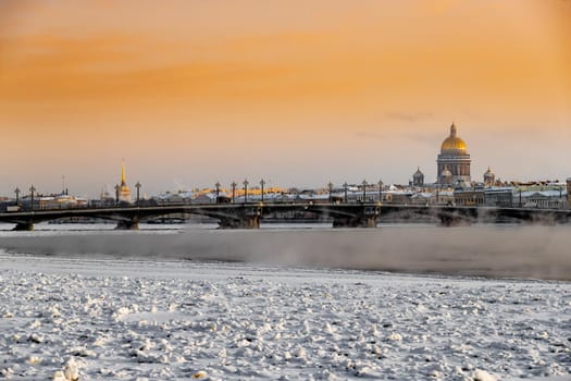 Winter panoramic view of St. Petersburg at sunset, Isaac cathedral and Blagoveshenskiy bridge on background, steam over frozen Neva river, sky of orange color. High quality photo