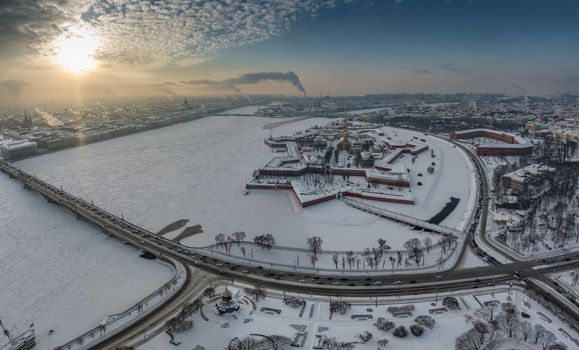 Drone point of view of winter St. Petersburg at sunset, frozen Neva river, steam over city, Peter and Paul fortress, car traffic on Trinity bridge, rostral columns, Palace drawbridge, panoramic view. High quality photo
