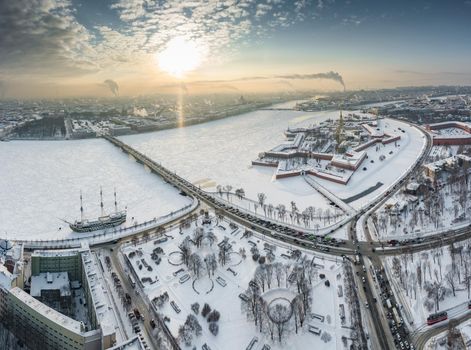 Drone point of view of winter St. Petersburg at sunset, frozen Neva river, steam over city, Peter and Paul fortress, car traffic on Trinity bridge, rostral columns, Palace drawbridge, panoramic view. High quality photo