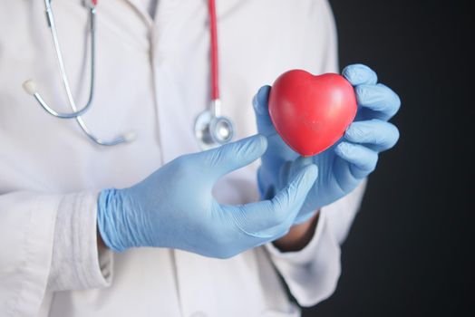 man hand in protective gloves holding red heart on blue .