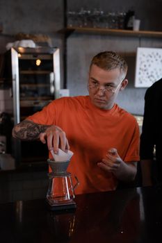 blonde guy in orange t-shirt preparing Alternative coffee brewing: chemex in modern loft coffee shop.