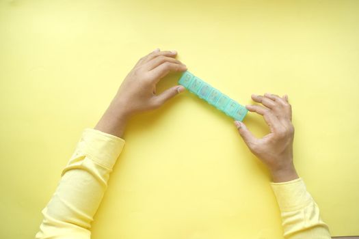 man's hands taking medicine from a pill box on yellow background .