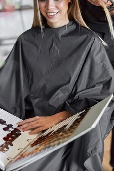 Blonde female client is chosing colour in book while hairdresser is choping her hair