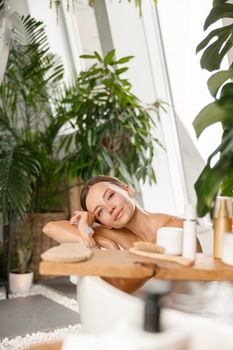 Peaceful young woman looking at camera while taking bubble bath at tropical spa resort. Wellness, beauty and care concept