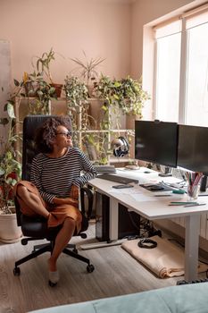 Smiling female person sitting in officer chair at desk with computers while working at home