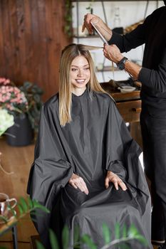 Confident male stylist is dyeing hair of blond caucasian female client