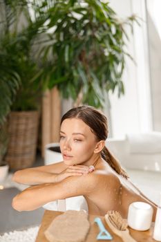 Portrait of pretty young woman taking bath and looking away, leaning on bathtub side. Wellness, beauty and care concept