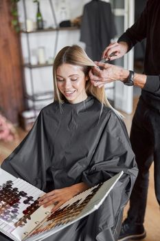 Blonde female client is chosing colour in book while hairdresser is choping her hair