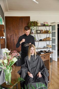 Confident male stylist is dyeing hair of blond caucasian female client