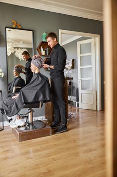 Happy beautiful light hair caucasian woman at beauty salon. Male master is drying her hair