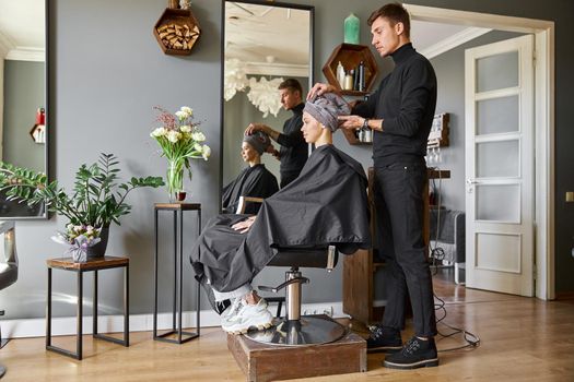Happy beautiful light hair caucasian woman at beauty salon. Male master is drying her hair