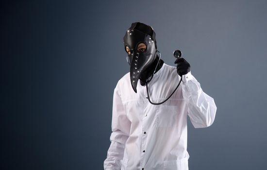 doctor in a dressing gown wearing a plague doctor mask with a stethoscope in his hands