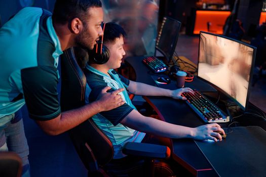 Happy esports player concentrated on game wearing wired headset while friend assisting him to pass network game in internet club