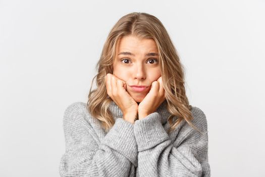 Close-up of cute and silly blond girl, wearing grey sweater, looking with admiration and sympathy at something beautiful, white background.